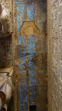 Dendera temple or Temple of Hathor. Painted columns with goddess faces and hieroglyphic ceiling of the hypostyle hall, ancient sandstone architecture with detailed carvings and blue painted astronomic