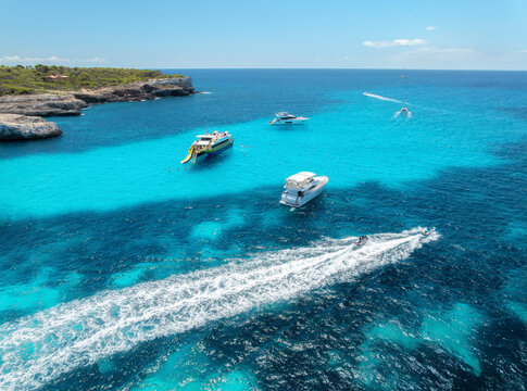 Aerial drone view of yachts and boats anchored in turquoise bay with rocky cliffs, caves, green trees, coastline in Mallorca island, Spain. Clear sea, sunny day. Seascape. Top view. Summer travel