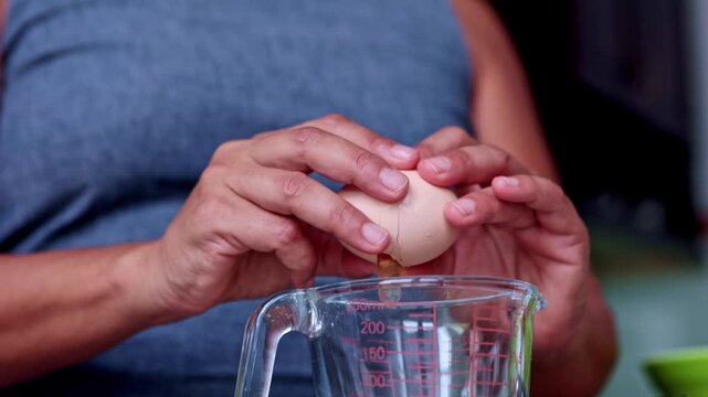 Person cracking fresh egg into a measuring cup