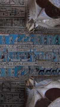 Dendera temple or Temple of Hathor. Painted columns with goddess faces and hieroglyphic ceiling of the hypostyle hall, ancient sandstone architecture with detailed carvings and blue painted astronomic