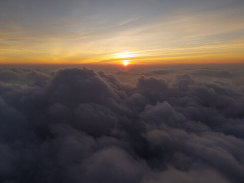 Aerial view of the sunset over the clouds near Mount Sindoro and Mount Sumbing, with golden light illuminating the horizon in Kecamatan Kedu, Jawa Tengah, Indonesia.