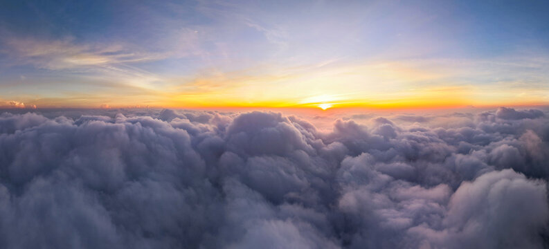 Aerial view of the Sindoro Sumbing mountains rising above a dense sea of clouds during a vibrant sunrise in Kecamatan Kedu, Jawa Tengah, Indonesia.