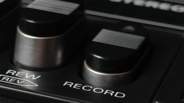 Macro perspective of a finger pushing the record button on a vintage cassette deck. The textured black key and silver trim highlight the retro audio recorder.