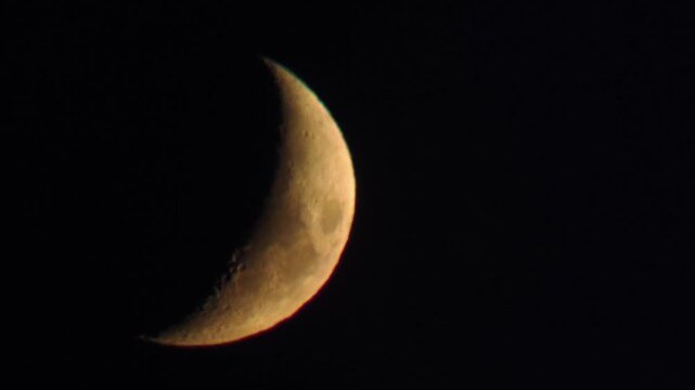 The orange crescent moon glows vibrantly against a black sky, revealing detailed craters along the terminator. Concept of astronomy, mystery, and the peaceful beauty of the cosmos.