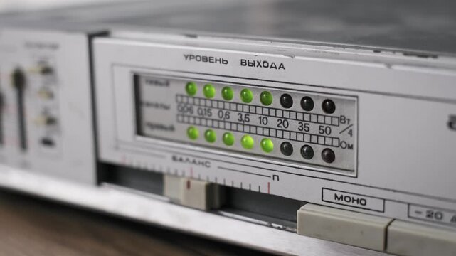 Angled close-up of a vintage analog amplifier with a working LED meter on a worn faceplate. The green and red lights show signal peaks suggesting heavy use in a recording studio.