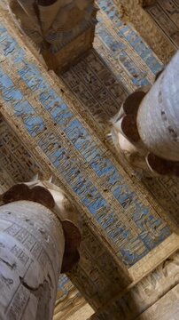 Dendera temple or Temple of Hathor. Painted columns with goddess faces and hieroglyphic ceiling of the hypostyle hall, ancient sandstone architecture with detailed carvings and blue painted astronomic