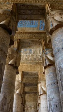 Dendera temple or Temple of Hathor. Painted columns with goddess faces and hieroglyphic ceiling of the hypostyle hall, ancient sandstone architecture with detailed carvings and blue painted astronomic