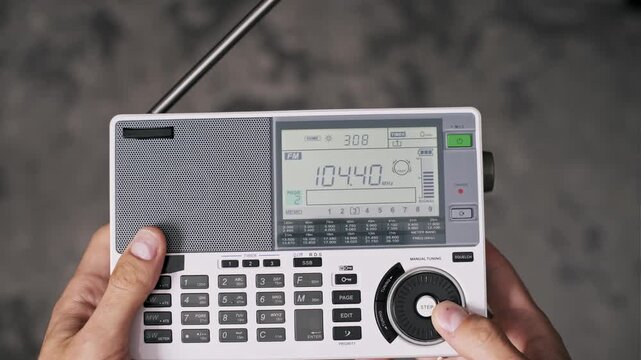 Male hands hold a white portable radio and turn the dial to tune the FM frequency on the LCD screen. Concept of searching for a broadcast signal or listening to news.
