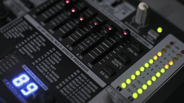 Close-up of a professional audio mixer with fluctuating LED level meters and EQ sliders. This equipment represents music production, live broadcasting, and sound engineering concepts.