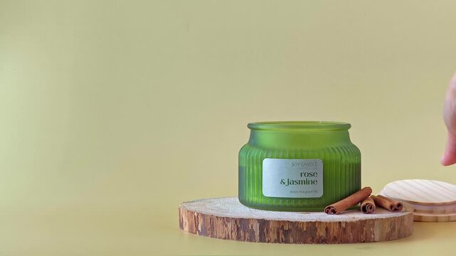 Female hand lifting a wooden lid off a luxury scented candle in a semi-matte green ribbed jar. Elegant home decor and wellness aesthetic.