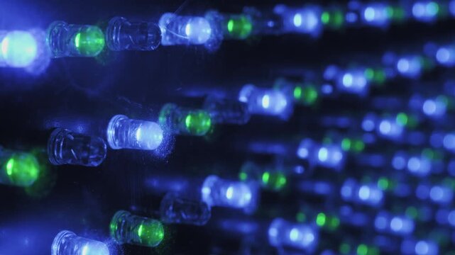 Angled macro perspective of an RGB LED panel showing rows of red, green, and blue diodes flickering in sequence. The shot features sharp foreground focus and soft background bokeh.