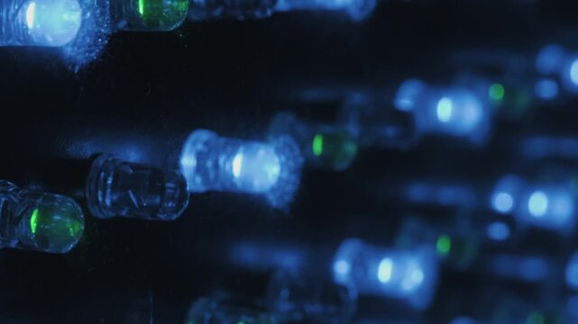 Macro side view of blinking colorful LED lights on a panel. Rows of red, green, and blue diodes appear with a shallow depth of field, creating a vibrant, technological, abstract background.
