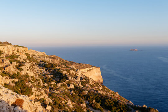 Rugged limestone cliffs sloping down to the Mediterranean sea with Filfla island in the distance in golden light at Dingli Cliffs, Malta