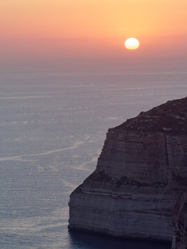 Vertical shot of a brilliant setting sun over the sheer limestone drop during a serene evening golden hour at Dingli Cliffs, Malta