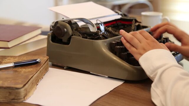Writer typing on an old typewriter on the desk with a cup of coffee and books.