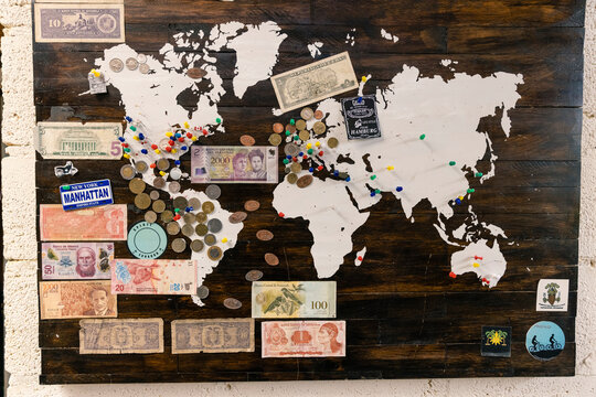 Travel Destinations Tracked on a Wooden Wall Map with Multi-colored Pins, Cash Bills and Collectible Coins.