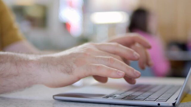 Hands type on laptop keyboard. Focus on fingers moving quickly. Background blurred with people nearby. Suggests work, communication, or online activity. Ideal for business, education, or tech themes
