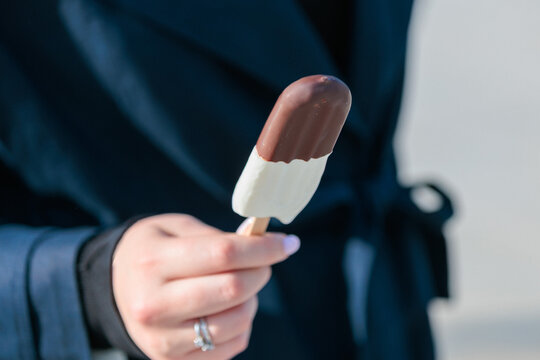 woman holds a chocolate and vanilla ice cream bar in her hand