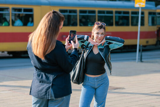 Young woman taking photo of friend with smartphone