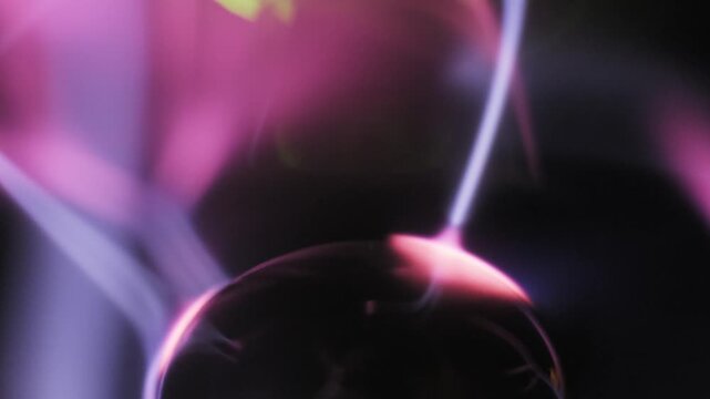 Extreme close-up of a moving plasma globe electrode emitting pink and purple electric streamers. Green light appears as ionized gas tendrils move inside the sphere.