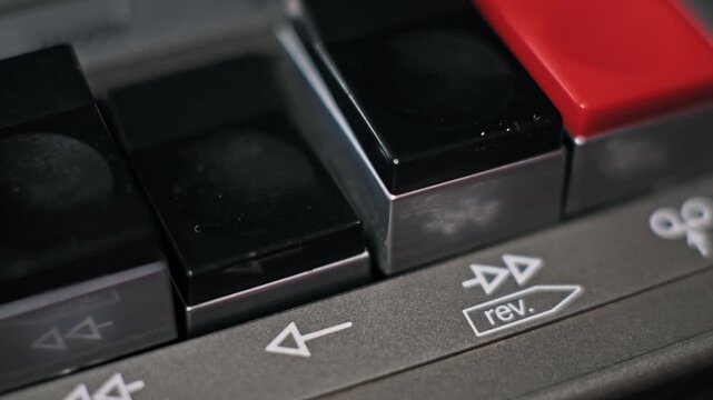 Extreme close-up of a female finger with brown nail polish pressing the play button. The button clicks on the retro cassette recorder to activate the tape playback.