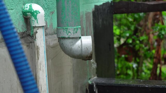Rainwater Flowing from House Drain Pipe During Heavy Monsoon Rain. Monsoon Rainwater Pouring from Roof Drainage Pipe in Residential Home. Roof Gutter During Monsoon Rainfall.