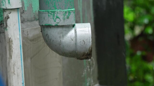 Rainwater Flowing Out of Plastic Gutter Downspout Pipe Exterior Footage. PVC Plumbing Drainage Pipe. Rainwater Drainage from Domestic Plastic Roof Gutter Spout System.