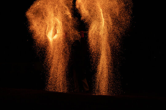 Silhouetted Fire Dancer Creating Orange Sparks at Night