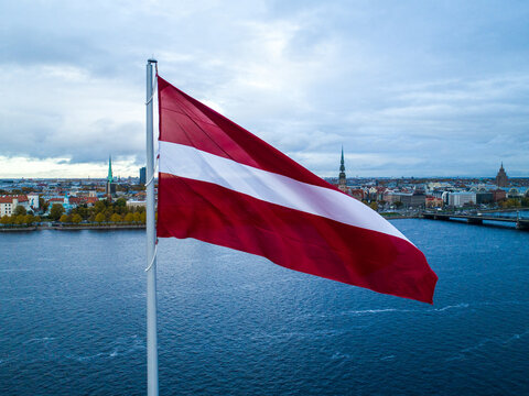 Aerial view of the Latvian flag waving on a flagpole with the historic Riga cityscape and Daugava river in the background in Riga, Latvia.