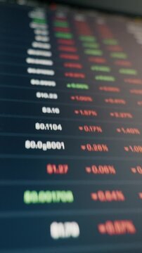Cryptocurrency exchange data with fluctuating prices and percentages scrolls on a monitor. Close-up, angled shot uses a shallow depth of field to highlight the numbers.