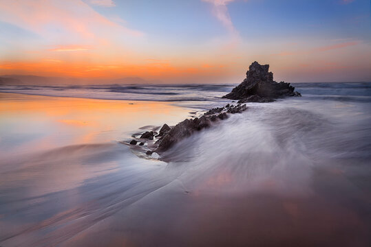 Beautiful long exposure seascape of flysch rock formations at Sopelana beach during a colorful sunset with silky water in the Basque Country, Spain