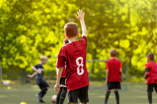 Young Football Player Raising Hand: Boy in Red Jersey Number 8 from Back View on Field