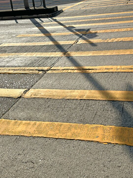 Sunlight casts long shadows across a worn pedestrian crossing with yellow stripes