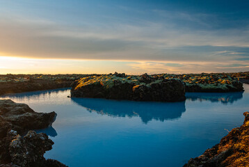 Fototapeta premium Volcanic lava formations beside the Blue Lagoon in Iceland with vivid moss colorful geothermal landscape and crystal blue water