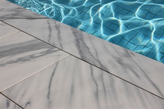 Luxurious grey and white marble tiles bordering a sparkling clear blue swimming pool water surface