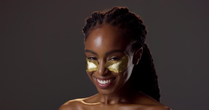 Gold, eye pad and portrait of black woman with skincare for natural beauty, product and luxury cosmetics in studio. Dermatology, smile and girl with collagen, patch or healthy skin on dark background