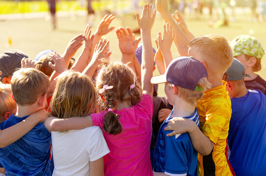 Children Team Huddle: Group of Kids Cheering and Raising Hands Together Outdoors. Kids Football Team Unity: Group of Boys and Girls Huddling Before Sports Match