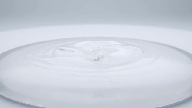 Transparent hydrogel gel slow-motion transformation with ripples on white surface showing high viscosity fluid dynamics in a continuous macro cinematic shot video footage