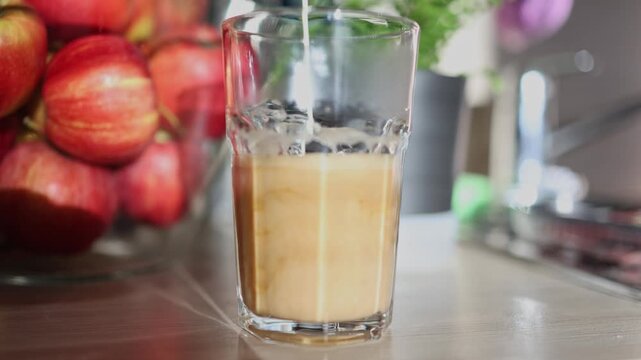 Fresh cream pours into black coffee inside transparent glass creating smooth swirling patterns and rich creamy texture during coffee preparation