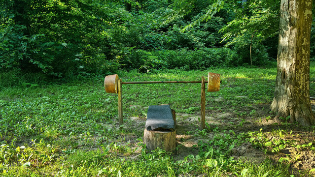 Rustic outdoor bench press with homemade barbell in forest clearing. Outdoor fitness equipment photography