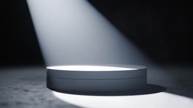 A minimalist white cylindrical pedestal sits on a textured concrete surface illuminated by a single dramatic spotlight from above creating a stark contrast and a sense of focus