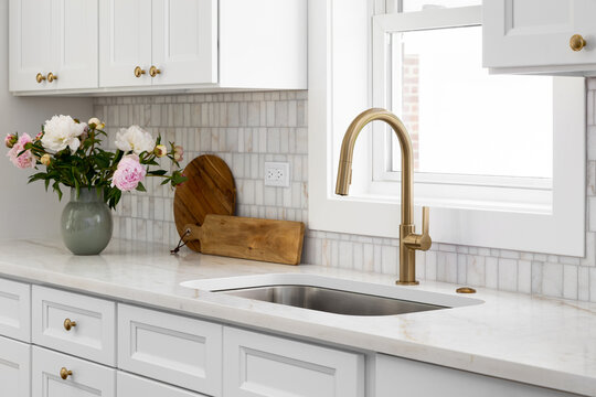 A kitchen detail with white cabinets, gold faucet, marble tiled backsplash, and a granite countertop.