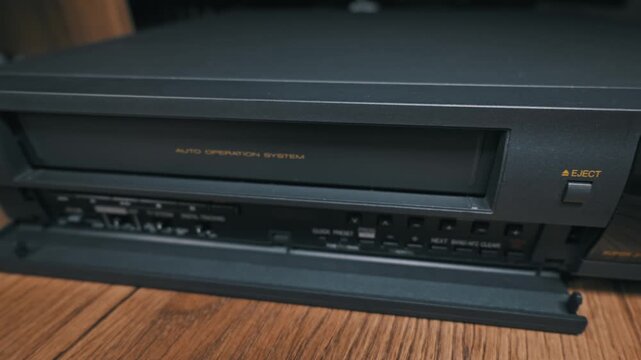 A person presses the eject button on a vintage VCR and removes the black VHS tape. Concept of retro entertainment, analog technology nostalgia, and classic home media experiences.