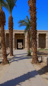 Seti I mortuary temple entrance with palm tree alley and ancient stone ruins in Luxor Egypt. Scenic pathway under vivid blue sky.
