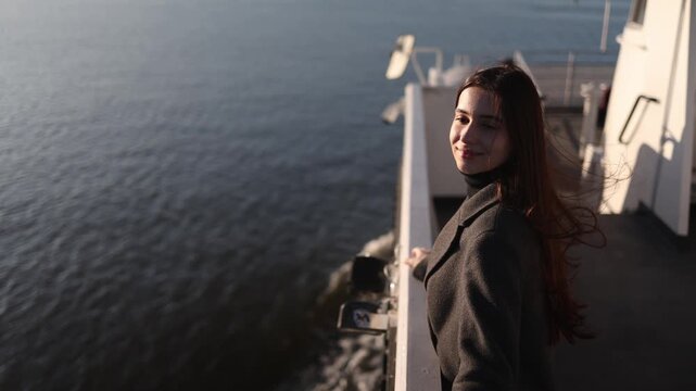 Young dark haired woman travels by ferry with sunlight illuminating her face against calm sea and endless horizon