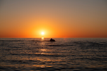 Obraz premium A jet ski sails across the sea at sunset.