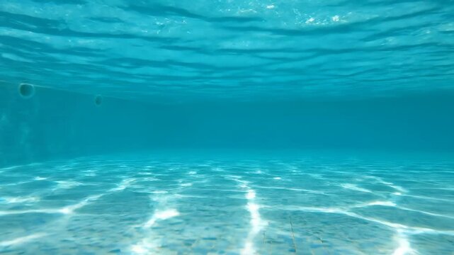 Crystal clear blue water underwater view in a bright swimming pool with sunlight reflecting and creating beautiful caustic patterns on the floor