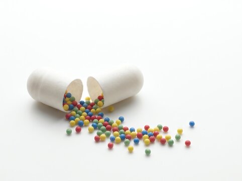 Open Medicine Capsule with Colorful Microgranules on White Background