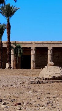 Seti I mortuary temple entrance with palm tree alley and ancient stone ruins in Luxor Egypt. Scenic pathway under vivid blue sky.