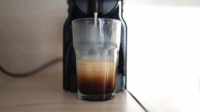 Automatic coffee machine fills clear glass with freshly brewed espresso creating smooth crema during coffee preparation process